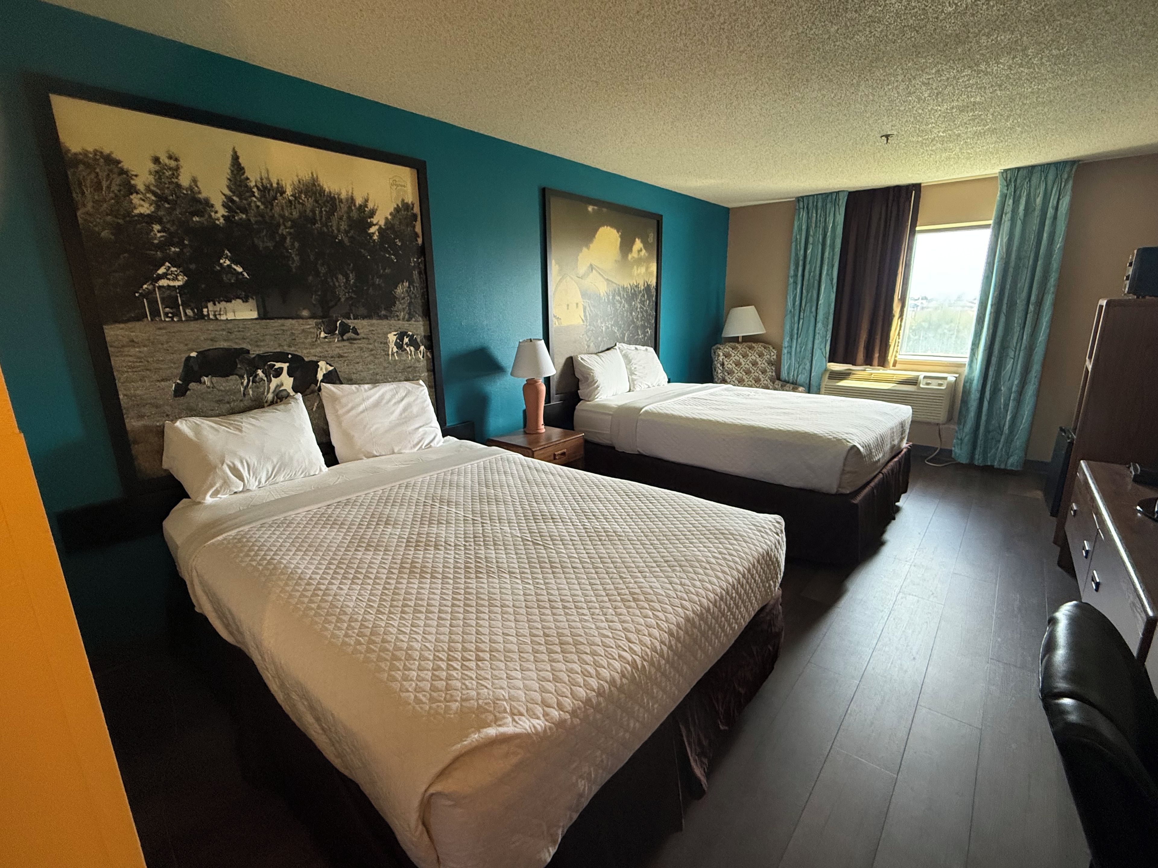 A hotel room with two beds, a desk, a chair, and artwork on the walls.