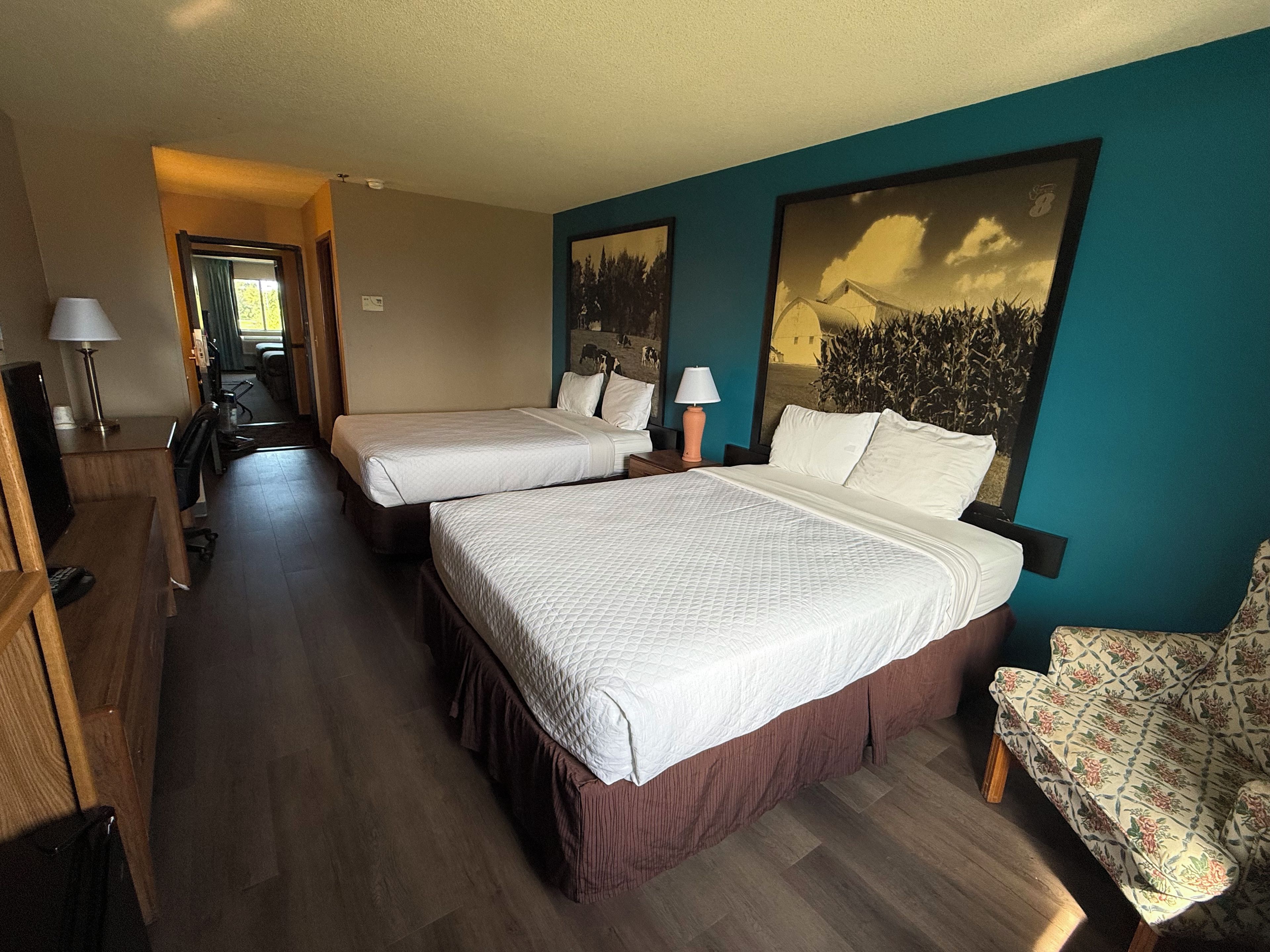 A hotel room with two beds, a desk, a chair, and a large window.