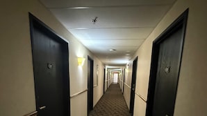 A hotel hallway with carpeted floors, dark doors, and wall-mounted light fixtures.