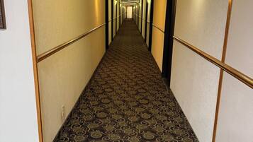 Pasillo de hotel con alfombra estampada, luces fijadas a la pared y puertas a ambos lados.