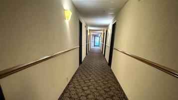 Ein Hotelgang mit Musterteppich, Wandleuchten und einer Tür am Ende.