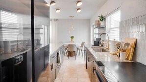 Una cuina moderna amb una illa central, electrodomèstics integrats i una zona de menjador amb taula rodona i cadires.