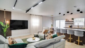 Un saló modern amb un sofà, una televisió i una zona de cuina amb tamborets.