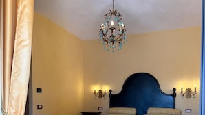 Quarto com cama grande, um banco, um candelabro e arandelas.