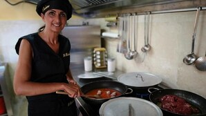Um cozinheiro vestido com uniforme preto cozinha em um fogão com várias panelas e frigideiras.