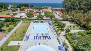 Una piscina con tumbonas y zona de juegos infantiles, rodeada de casas y vistas al mar.