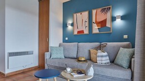 Una sala de estar moderna con un sofá gris, dos mesitas auxiliares y un cuadro abstracto en la pared.