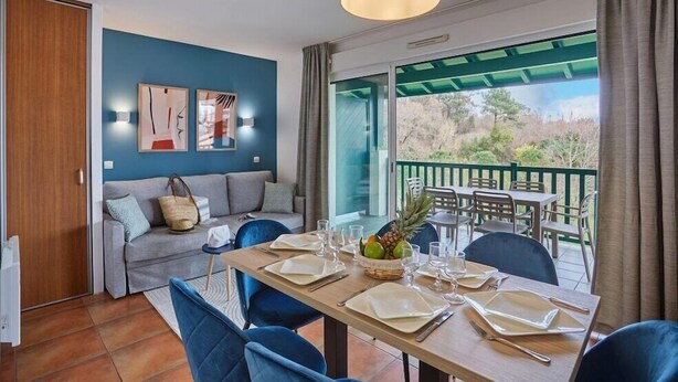 Un comedor con una mesa dispuesta para cuatro personas, un sofá y un balcón con mobiliario exterior.