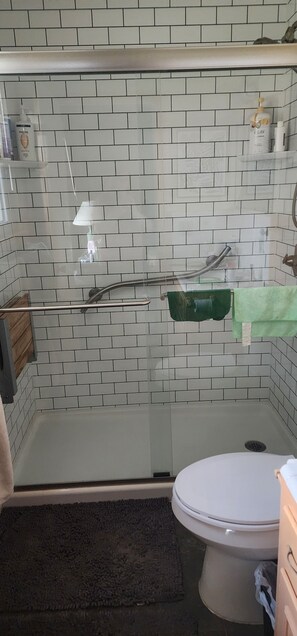 A bathroom with a glass-enclosed shower, white tiled walls, a toilet, and a green towel rack. - Serene 3-bedroom house with AC in vibrant Austin easy access to downtown (Austin)