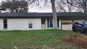 A single-story house with a garage, a tree in front, and a parked car. - Serene 3-bedroom house with AC in vibrant Austin easy access to downtown (Austin)
