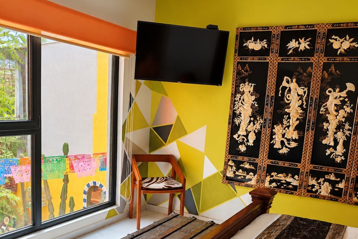 Ein Schlafzimmer mit einem Bett, einem Sessel, einem Fernseher und einem Fenster mit Gartenblick.