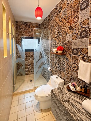 Une salle de bain avec des carreaux décorés, des toilettes, une douche avec une porte en verre et un luminaire suspendu rouge.