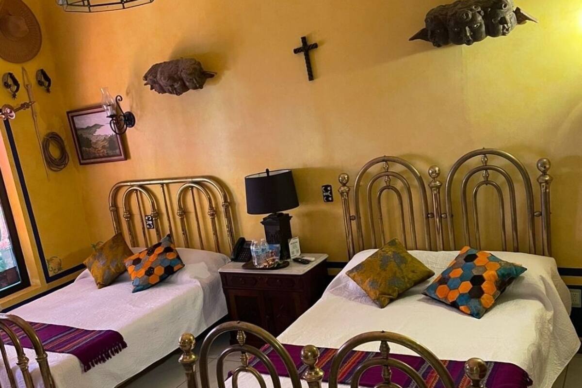 Een kamer met twee bedden, een nachtkastje met een lamp, een kruis aan de muur en een plank met decoratieve voorwerpen.
