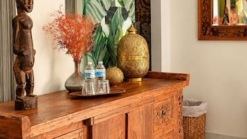 Un mueble de madera con intrincados grabados, un espejo con marco geométrico y una planta grande de hojas anchas.