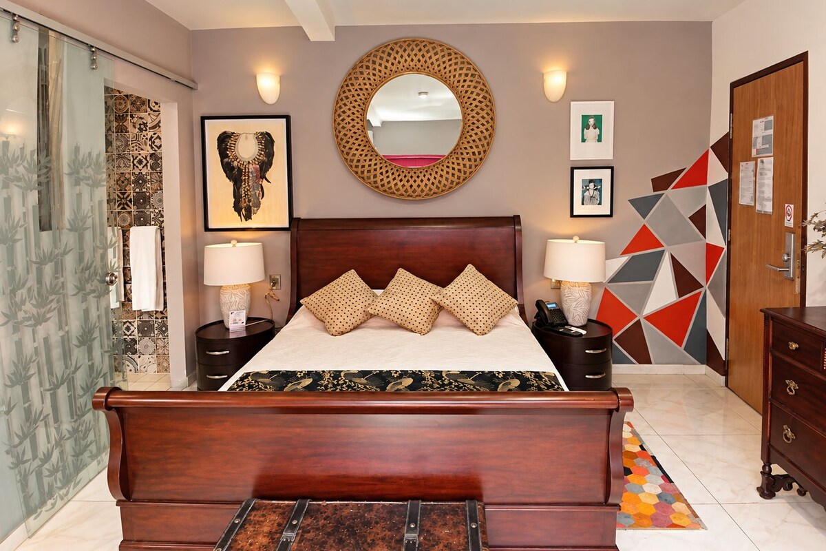 A bedroom with a wooden bed, two bedside tables with lamps, a round mirror, and a geometric-patterned wall.