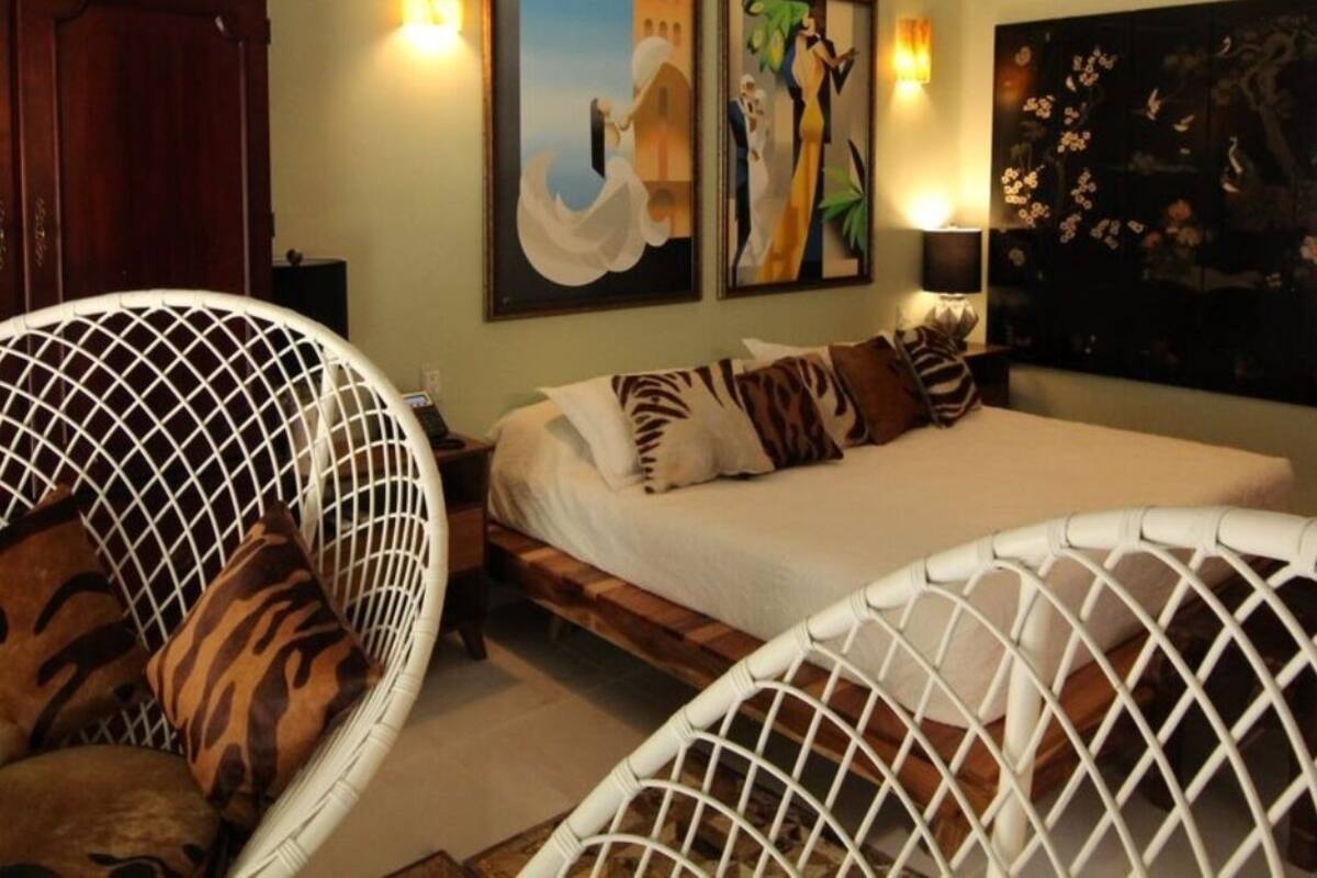 Een slaapkamer met een bed, twee aan de muur bevestigde schilderijen, een plafondventilator en een hanglamp.