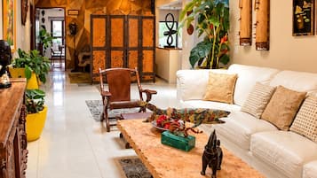 Una sala moderna con sofá, mesa de centro y objetos decorativos. Se observa un aparador de madera y una planta grande.