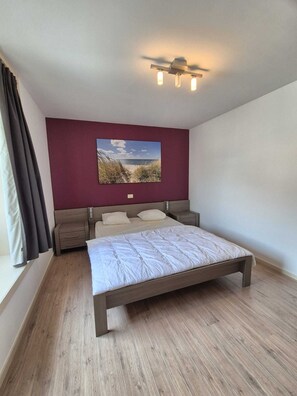 A bedroom with a wooden bed, a nightstand, a wall-mounted light fixture, and a large landscape painting above the bed. - Spacious duplex apartment- 8p - walking distance beach (Blankenberge)