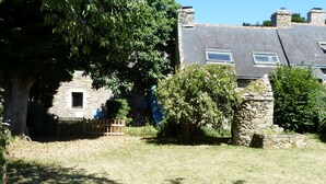Ein Haus aus Stein mit einem geneigten Dach, einem Holzzaun und einem großen Baum im Vordergrund.