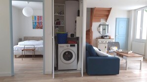 Ein gemütlicher, kleiner Wohnraum mit Bett, Waschmaschine, Sofa und einem kleinen Tisch.