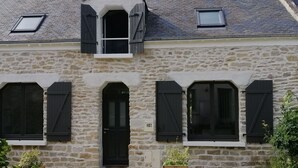Ein Steinhaus mit einer schwarzen Tür, drei Fenstern mit Fensterläden und einem kleinen Balkon.