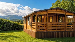 A wooden cabin with a porch, large windows, and a view of mountains.
