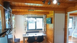 A wooden-paneled room with a dining table, two chairs, a window with curtains, a white door, and a ceiling light fixture.