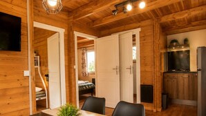 A wooden cabin interior with a dining area, kitchen, and a bedroom with a window.