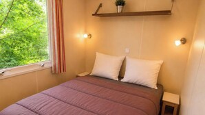 Une chambre à coucher avec un lit, des tables de chevet, une fenêtre avec des rideaux et une étagère avec une plante.
