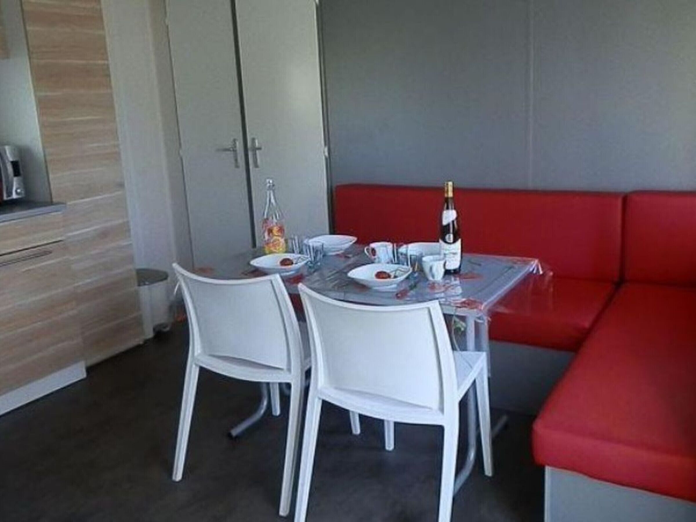 Un'accogliente zona pranzo con tavolo apparecchiato per due, una panca imbottita rossa e un angolo cottura con pensili.