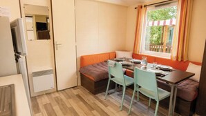 Une petite pièce comprenant un lit, une table avec des chaises, une fenêtre avec des rideaux, un radiateur et un téléviseur.