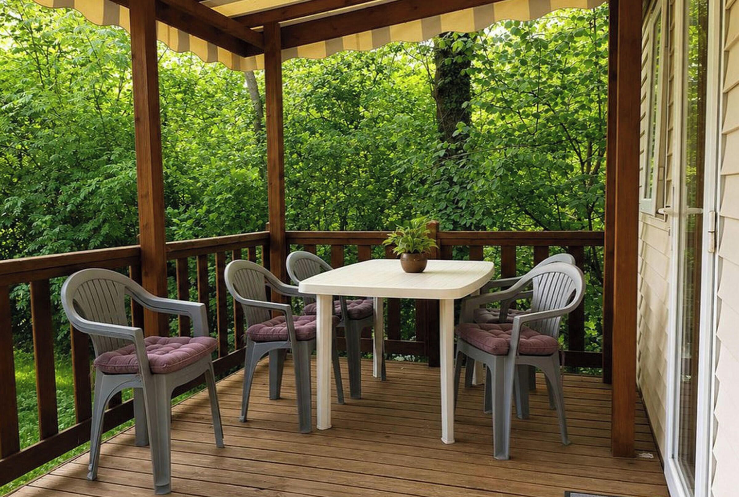 Una terrazza coperta all'aperto con tavolo e sedie, immersa nel verde.