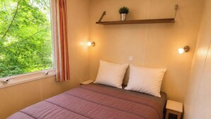 Une chambre à coucher avec un lit, des tables de chevet, une fenêtre avec des rideaux et une étagère avec une plante.