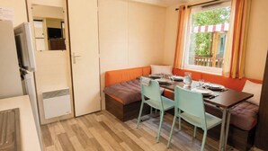 Une petite pièce comprenant un lit, une table avec des chaises, une fenêtre avec des rideaux, un radiateur et un téléviseur.