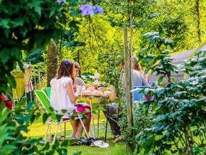 Ein Garten mit Tisch und Stühlen, umgeben von viel Grün und Bäumen.