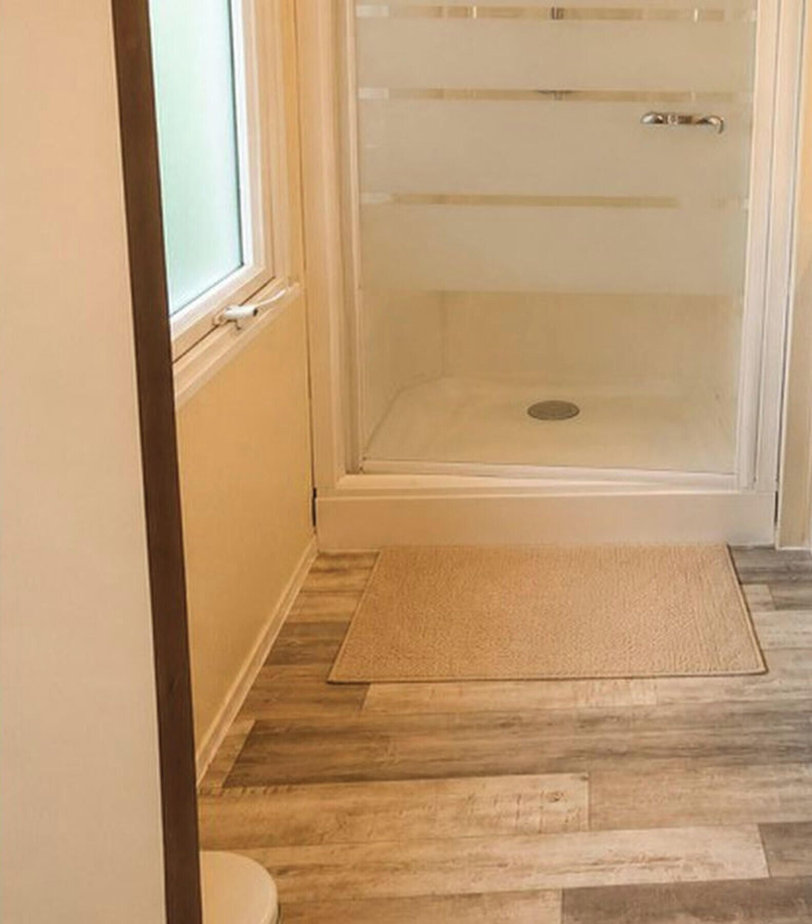 A bathroom with a shower, a toilet, and a wooden floor.