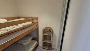 Habitación con literas y una pequeña estantería en la pared.