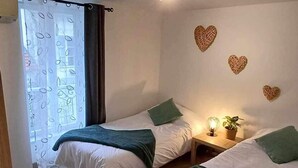 Ein Schlafzimmer mit zwei Betten, einem Fenster mit Vorhang und dekorativer Wandkunst in Herzform.