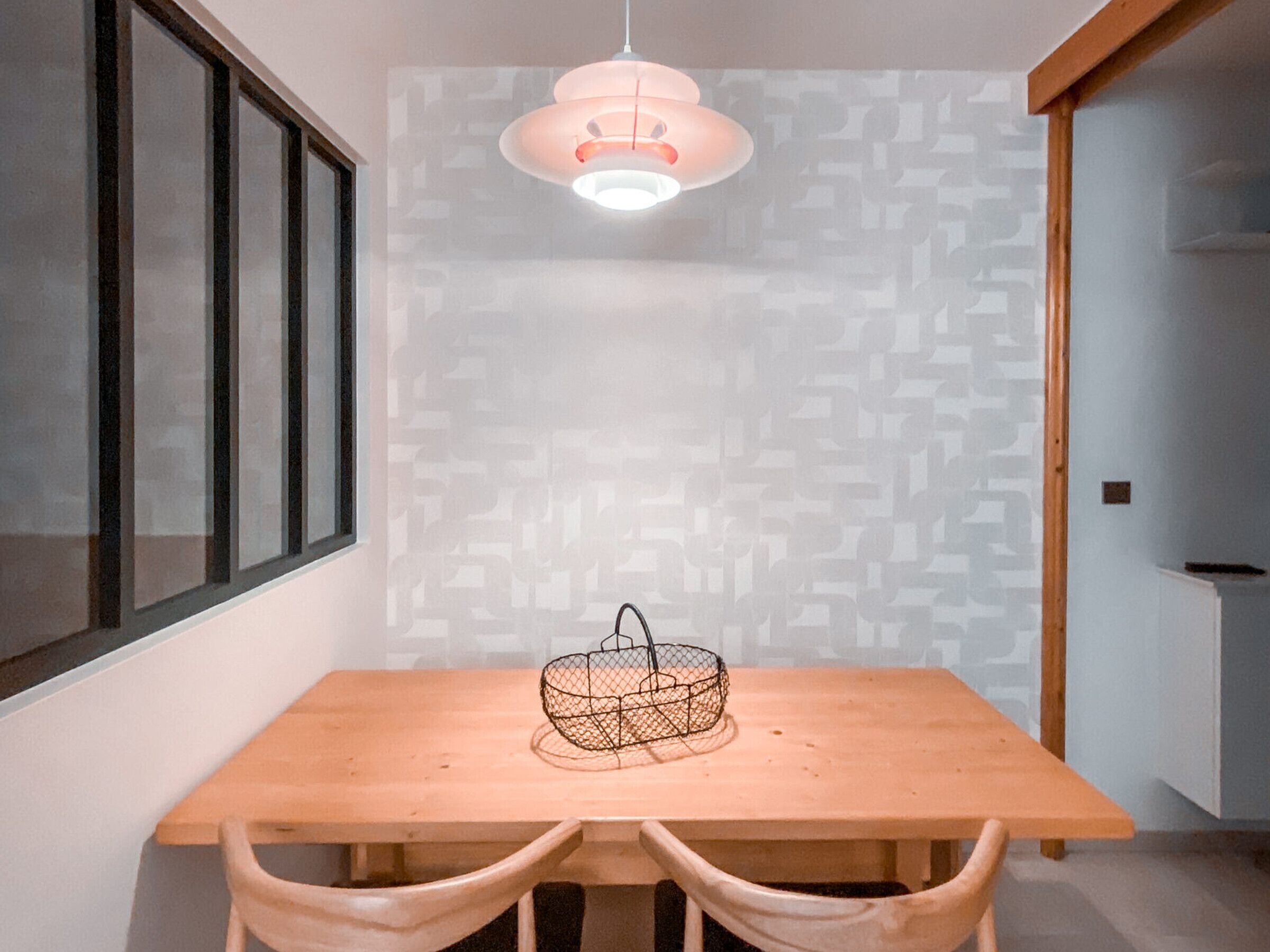 A dining area with a wooden table and chairs, a hanging light fixture, and a patterned wall.
