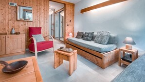 Una stanza accogliente con pavimento in legno, un divano, una poltrona rossa, un tavolino e una lampada.