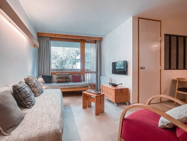 A cozy room with a sofa, a small table, a TV, and a window with curtains. - Apartment with mountain view - 4 guests (Val-d'Isère)