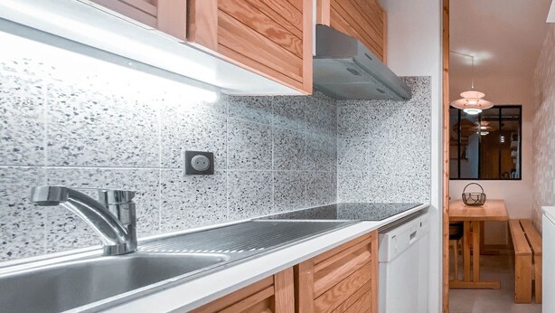 Una cucina moderna con lavello in acciaio inossidabile, mobili in legno e schienale decorato.