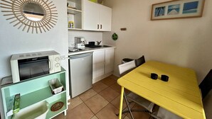 Eine kleine Küche mit Mikrowelle, Kühlschrank und Spüle. Ein gelber Tisch mit zwei Stühlen und eine kleine Ablagefläche mit Küchenutensilien.
