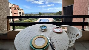 Ein Balkon mit Tisch für Zwei, mit Blick auf ein Schwimmbecken und Gebäude.