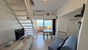 Un espai habitable compacte amb una escala cap a un balcó, una zona de menjador i un sofà.