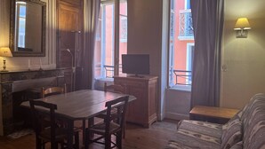 Ett mysigt vardagsrum med ett träpanelat tak, en matplats med bord och stolar, en soffa, en tv på ett träbord och ett fönster med gardiner.