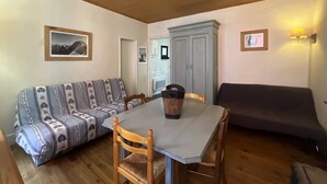 Ett mysigt rum med ett träpanelat tak, en soffa, ett matbord med stolar och ett skåp.