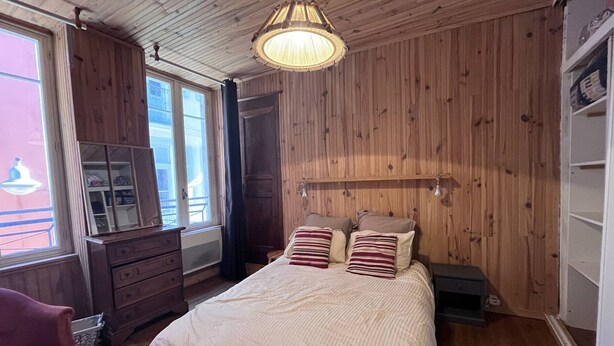 Ett sovrum med ett träpanelat tak, en säng med randiga kuddar, en byrå och ett fönster med utsikt över en balkong.