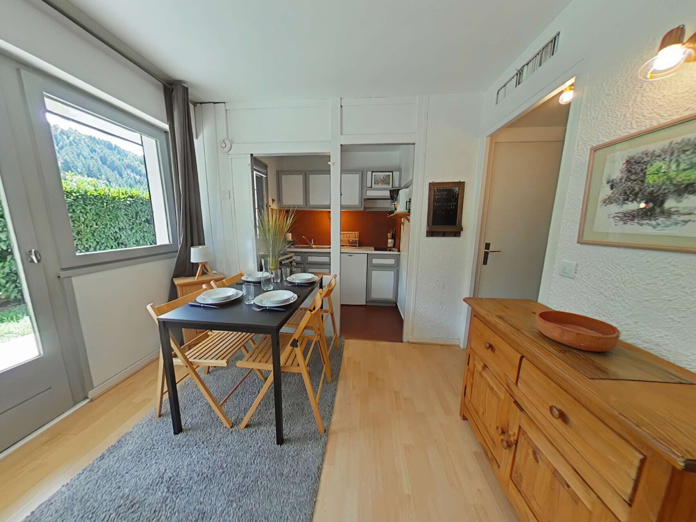 Een moderne keuken met witte kasten, een houten eettafel gedekt met borden, en uitzicht op een tuin door een groot raam.
