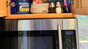 A kitchen cabinet with various food items, including paper towels, plates, and a box of Maxwell House coffee. - The Canopy Cabin a Nature Lovers Eclectic Treehouse (Athelstane)